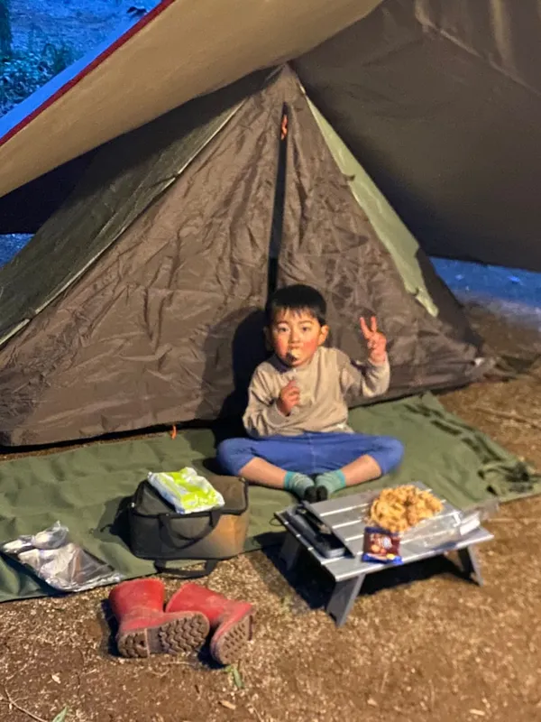 夜、タープの下のグランドシートに座る子どもと野営らしい設営