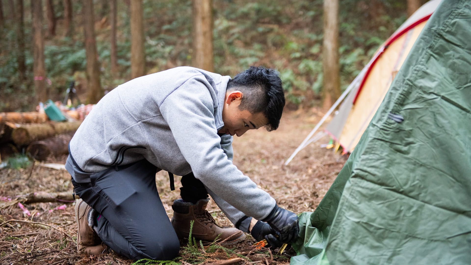 膝をついてテントのペグを打つ人と、張り終えた幕